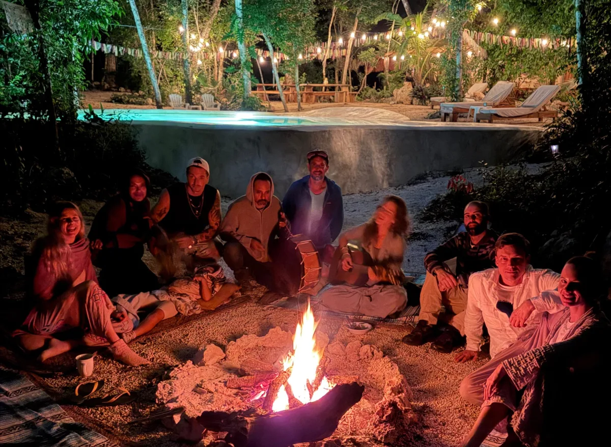 Friends and family gathered around the sacred bonfire — the cenote pool glowing behind