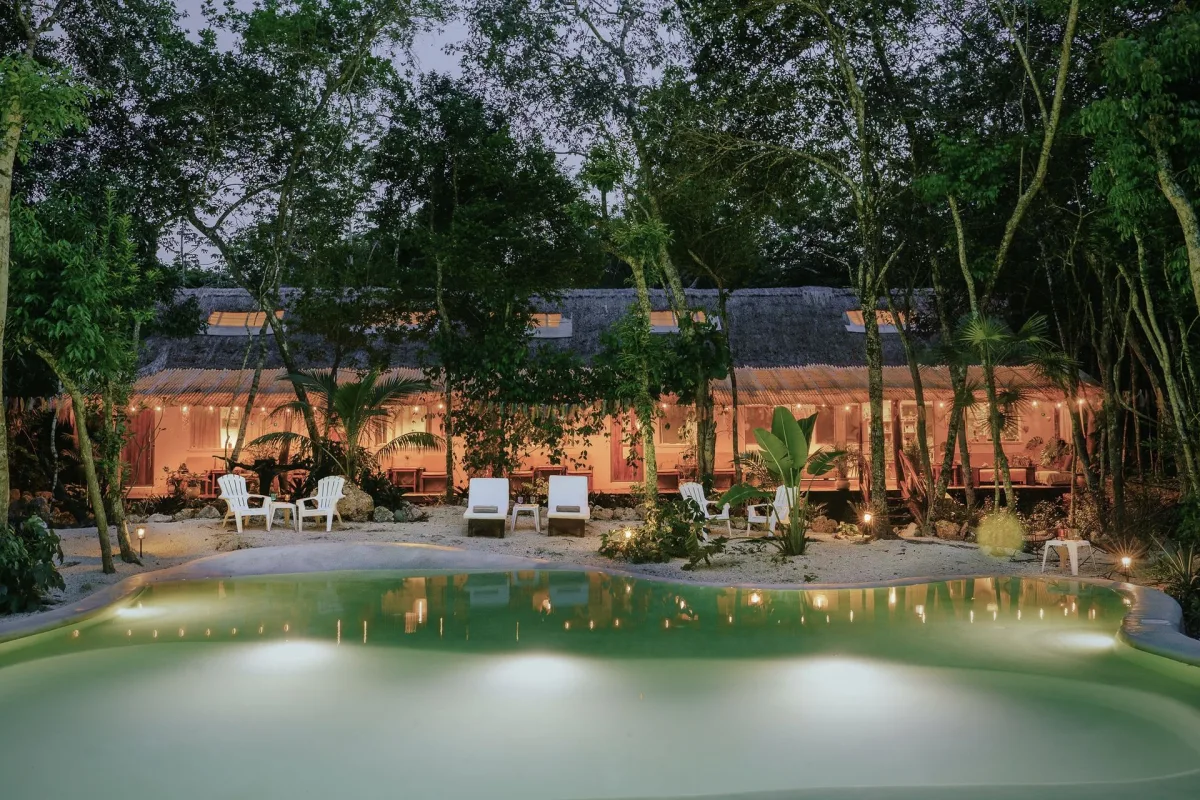 La alberca alimentada por cenote en Casa Arkaana al atardecer, rodeada por la selva de Tulum