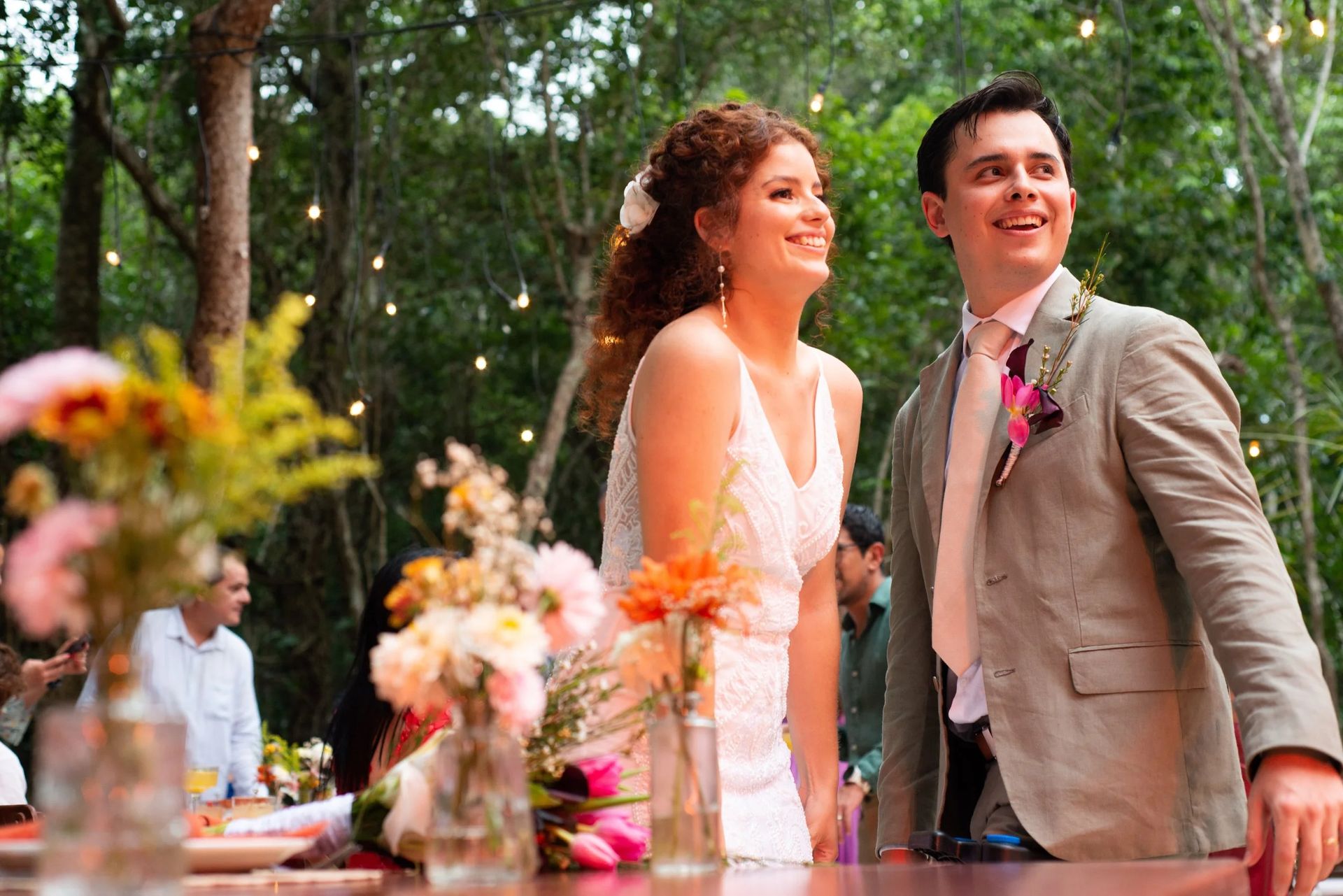 Bride and groom at the wedding dinner table, jungle and warm lights behind them